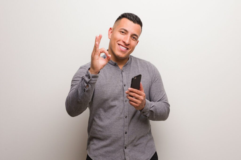 Photo of young professional man making the OK sign holding smart phone