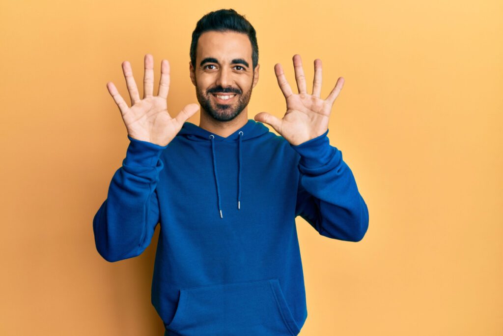 Image of male with dark hair and bear wearing hoodie holding up 10 fingers.